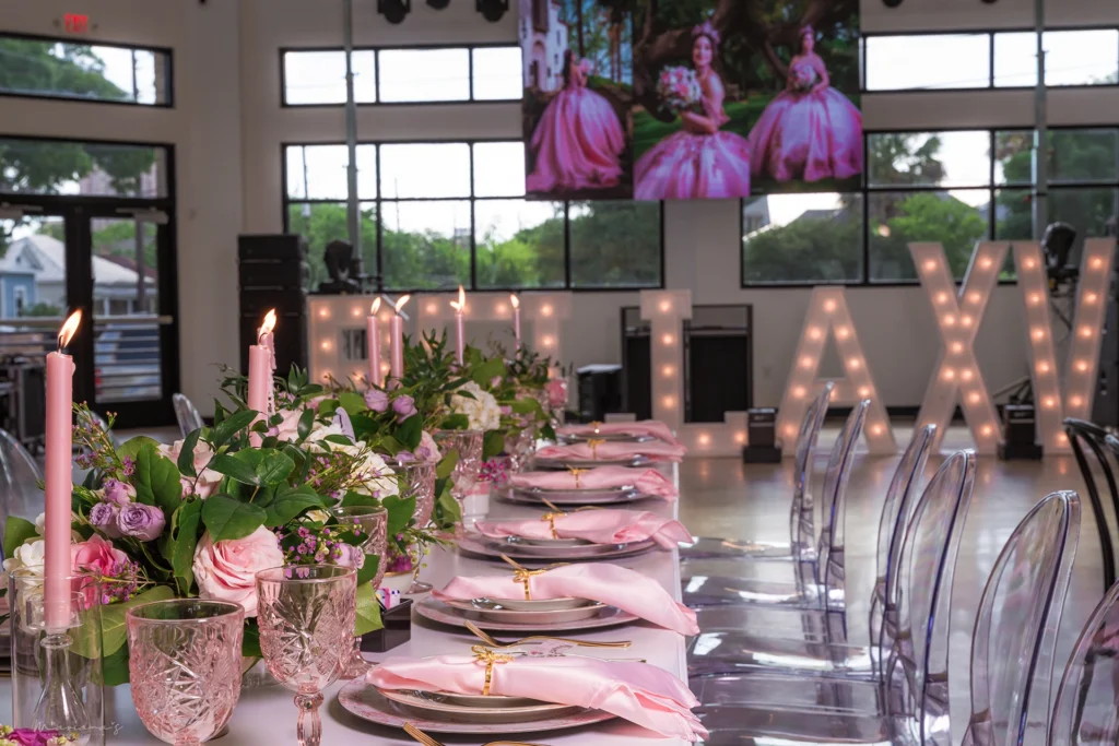 Pink place settings, candles and cups adorn the tables with a lighted Quinceanera sign in the background