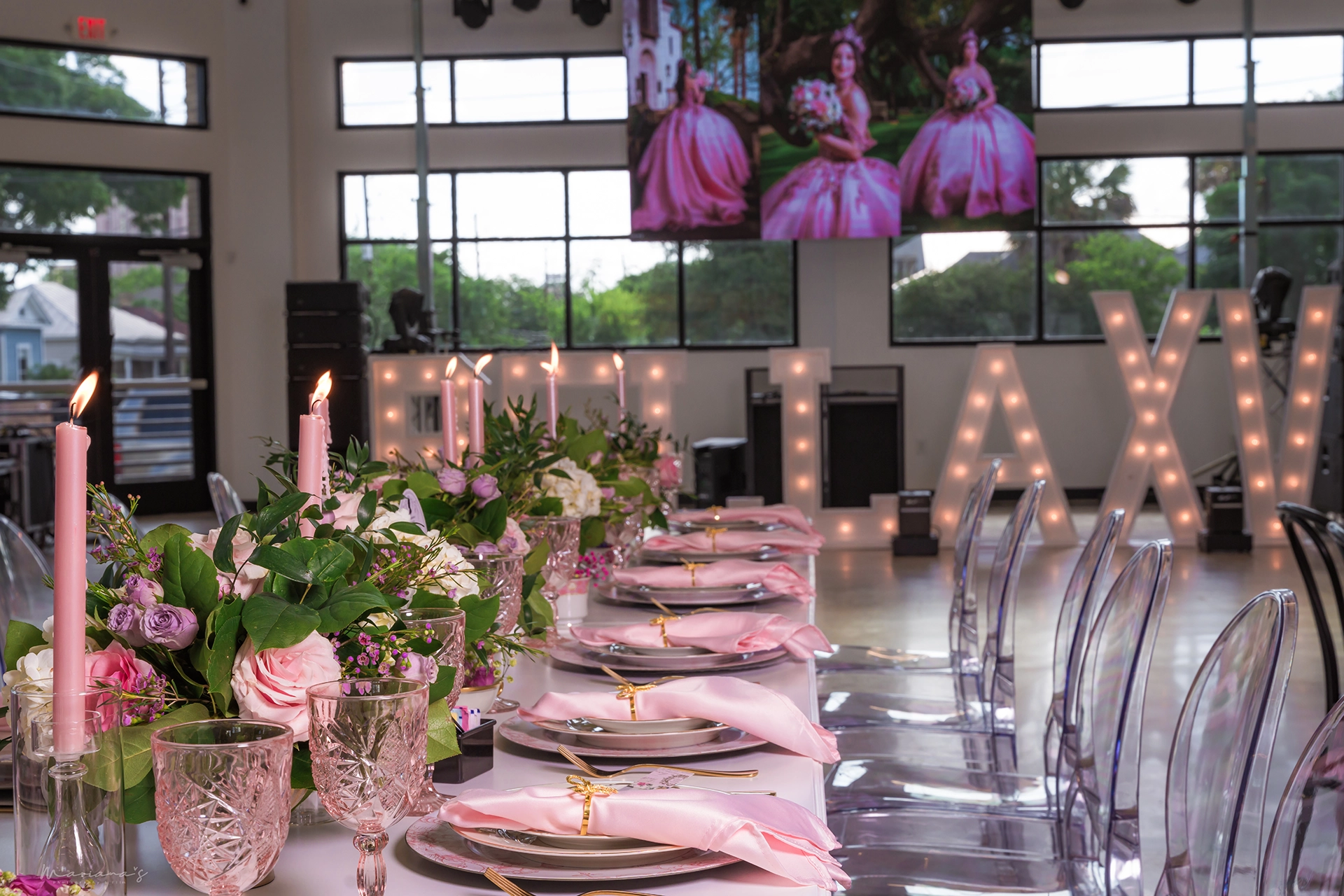 Pink place settings, candles and cups adorn the tables with a lighted Quinceanera sign in the background