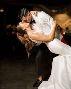 A bride and groom kiss as he dips her in a dimly lit room.