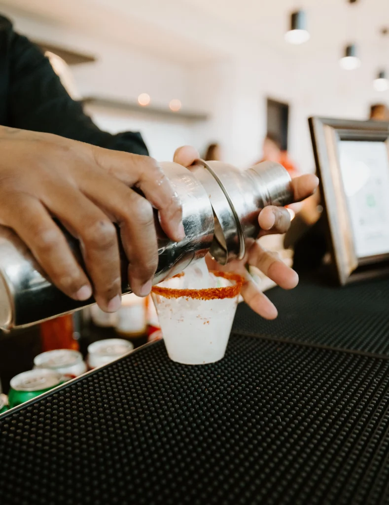 A drink is poured from a shaker into a cup with a seasoning on the rim