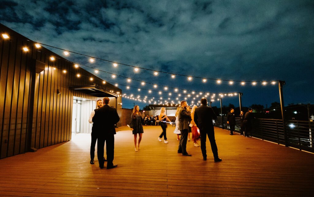 Partygoers mingle under string lights on the Skyline's outside deck event space.