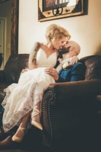 A bride sitting on the lap of her groom as they kiss.
