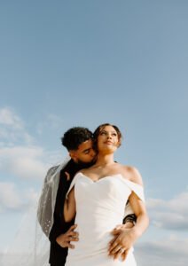 A bride is embraced behind by her new husband who gently kisses her neck.