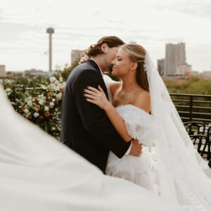 A bride and groom embrace. The San Antonio skyline is in the background